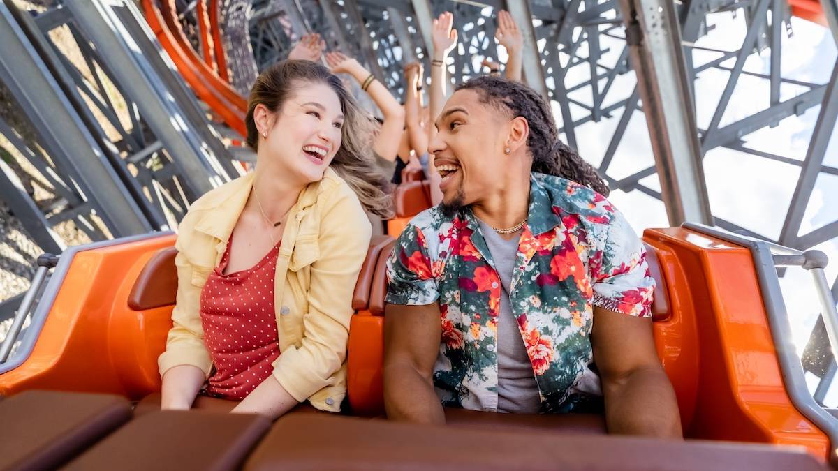 Two people smiling at each other as they sit in an orange roller coaster cart